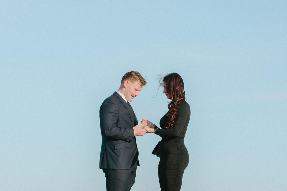 Professional business people in dark suits facing each other against a bright blue sky background.