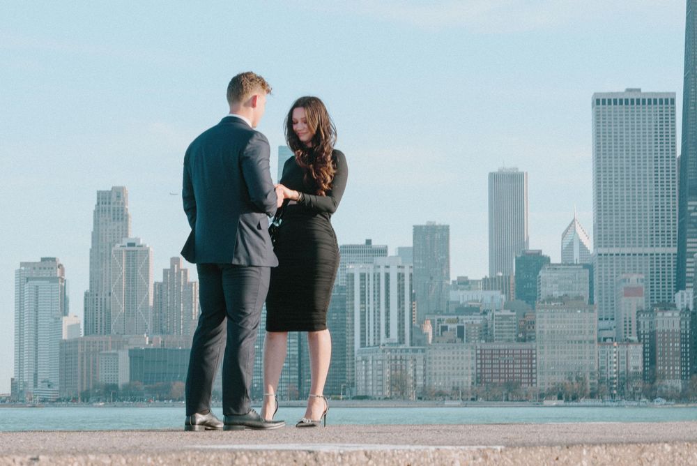 A couple stands together overlooking the Chicago skyline on a clear day from an observation point.
