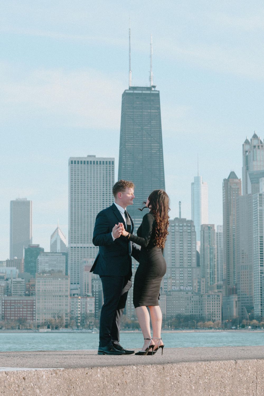 A couple shares a romantic moment against the backdrop of Chicago's skyline featuring the iconic John Hancock building.