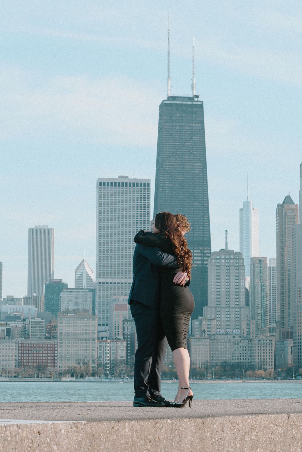 A couple embraces on North Avenue Beach with Chicago's iconic John Hancock Center and skyline in the background.