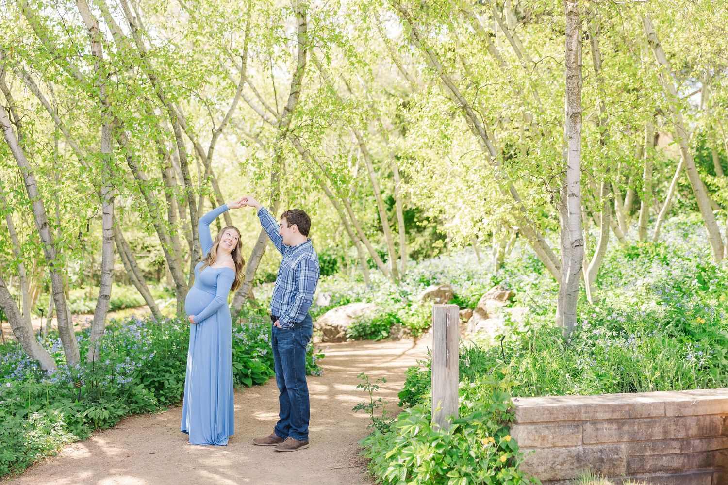 Couple shares a joyful moment together in a sunlit garden path surrounded by blooming spring flowers and greenery at Chicago Botanic Garden