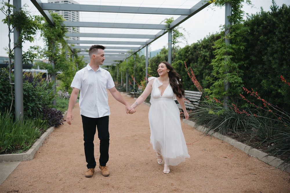 A couple strolls together on a path under a modern pergola surrounded by manicured gardens.