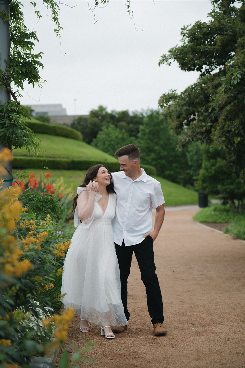 A couple walking together on a winding garden path with blooming flowers and lush greenery surrounding them.