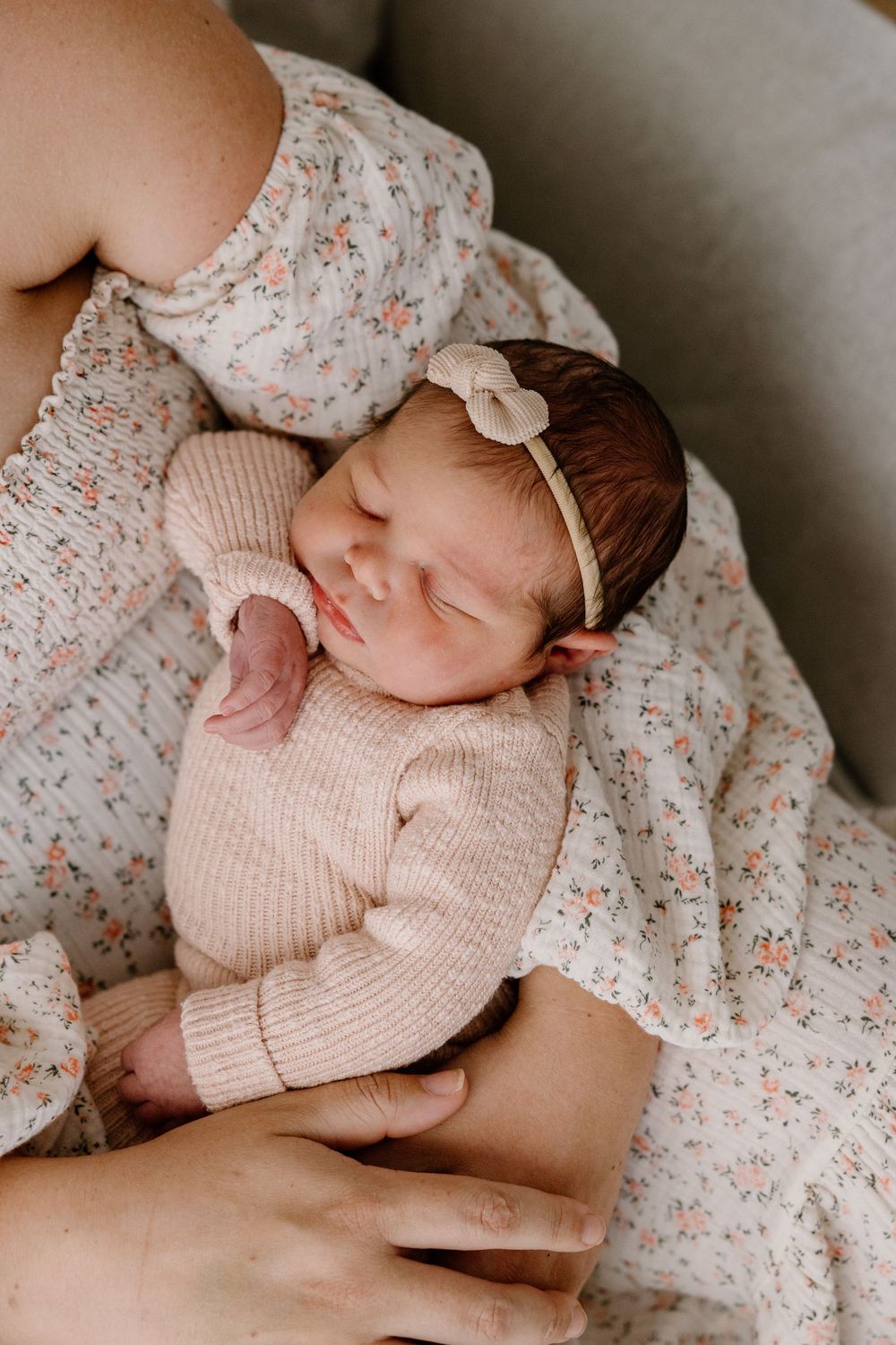 A newborn wearing a knit sweater lies on floral bedding while being gently held.