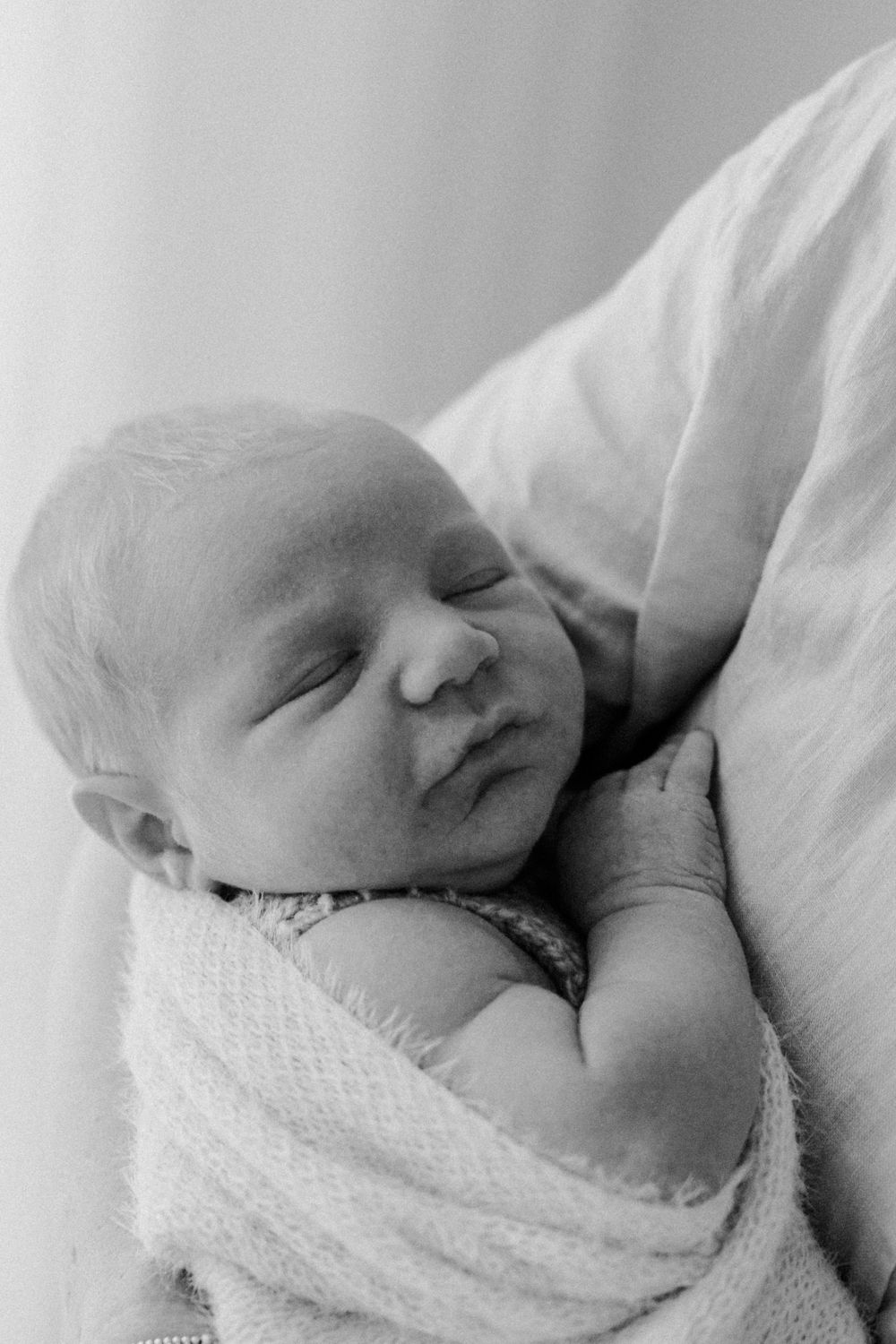 Peaceful sleeping newborn baby wrapped in soft white textured blanket captured in black and white photography.