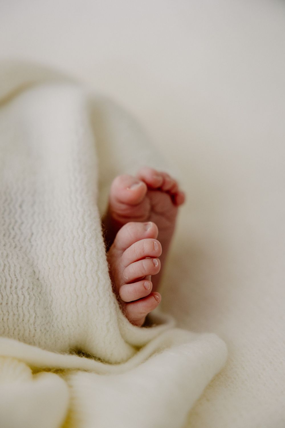 Close-up view of tiny baby feet peeking out from under a soft cream-colored knit blanket.