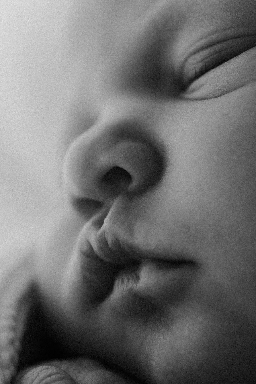 A close-up black and white photograph of a baby's nose and mouth in soft focus.