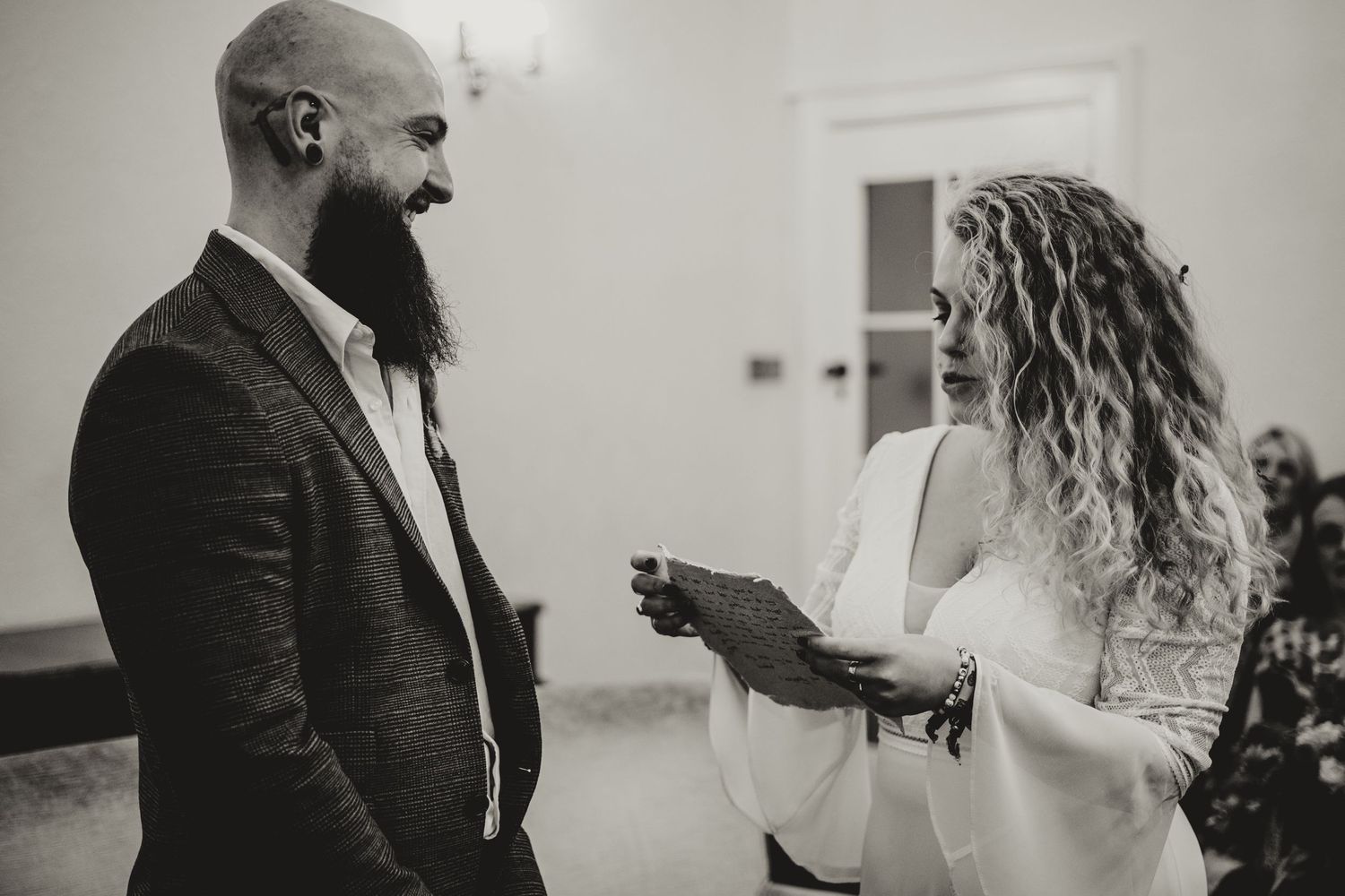 A couple exchange joyful expressions during their wedding ceremony while reading vows in black and white photography.