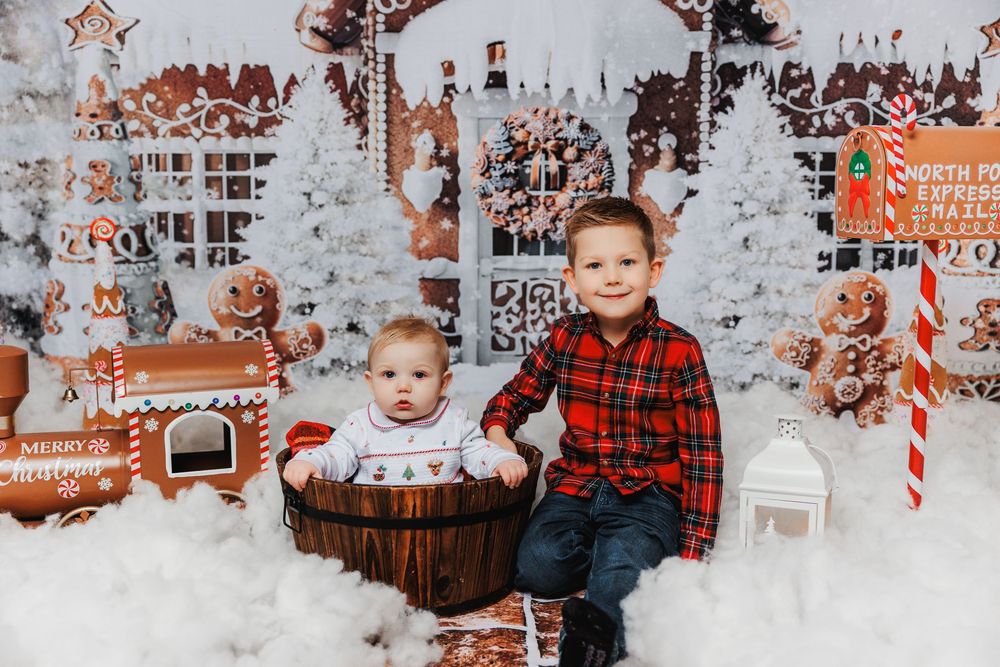 Holiday photo setup with plaid shirt, rustic barrel, white trees, lanterns and candy cane decorations surrounded by fake snow.