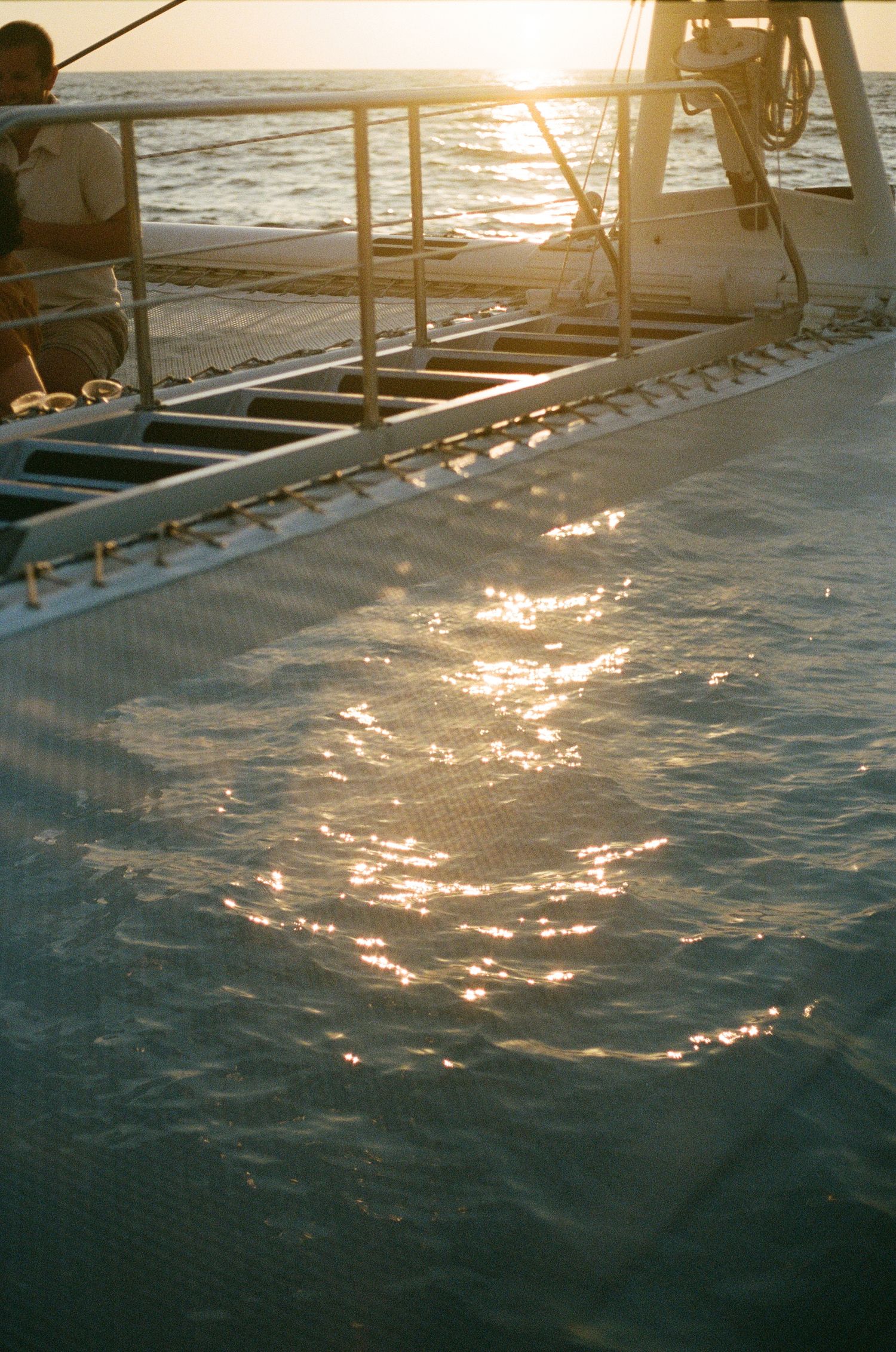 Sunset reflection on ocean water viewed from sailboat deck.