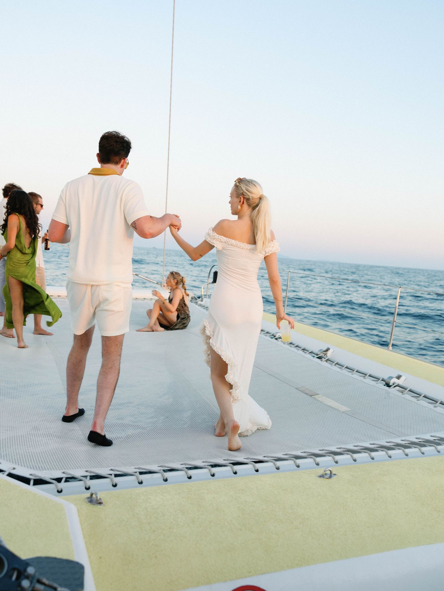 A couple in white outfits walking together on a boat deck with ocean views.