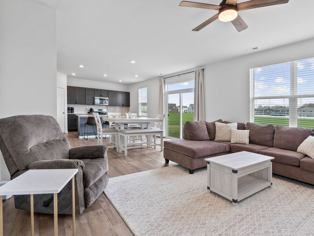 Open concept living room and kitchen with brown sectional, hardwood floors, and modern gray and white color scheme.