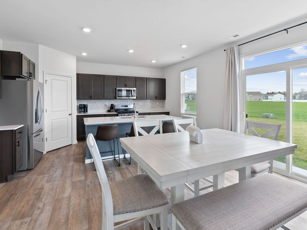 Modern open concept kitchen and dining area with white table, bench seating, and dark cabinets in new construction home.