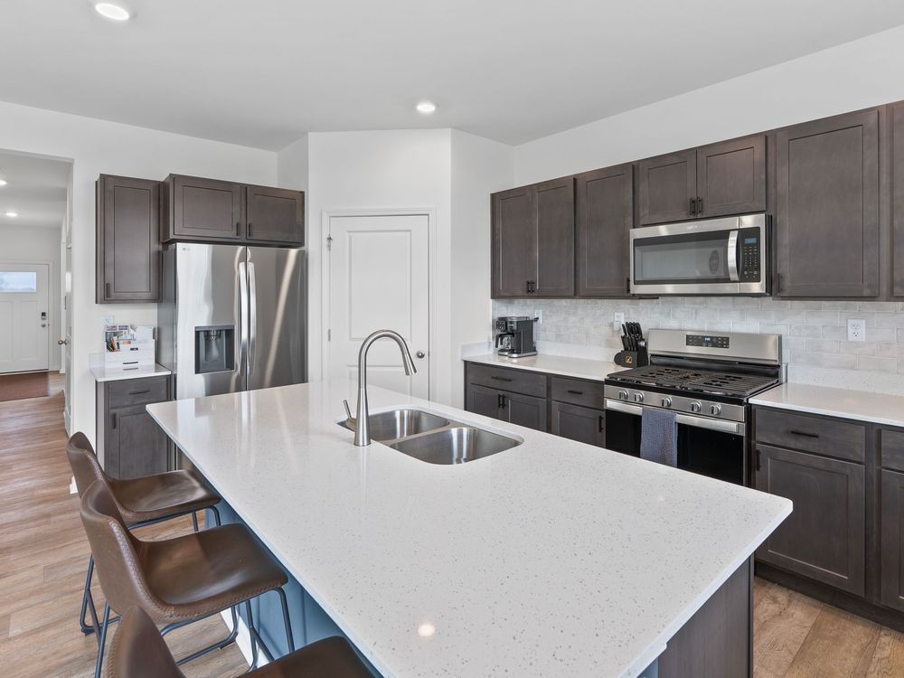 Modern kitchen interior with dark wood cabinets, white quartz countertops, and stainless steel appliances featuring a large island.