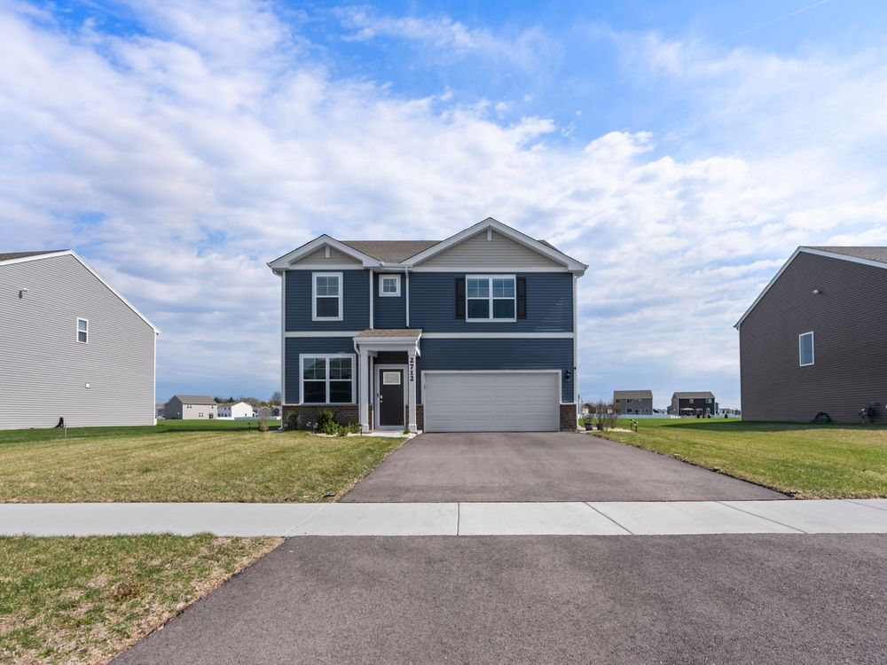 Modern two-story blue and gray home with attached garage and concrete driveway under partly cloudy sky.