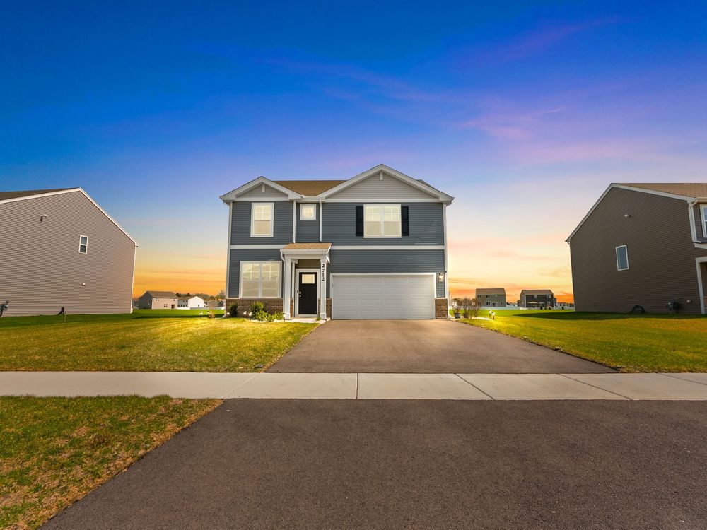A modern two-story suburban house with beige siding and attached garage at sunset against a vibrant blue and pink sky.