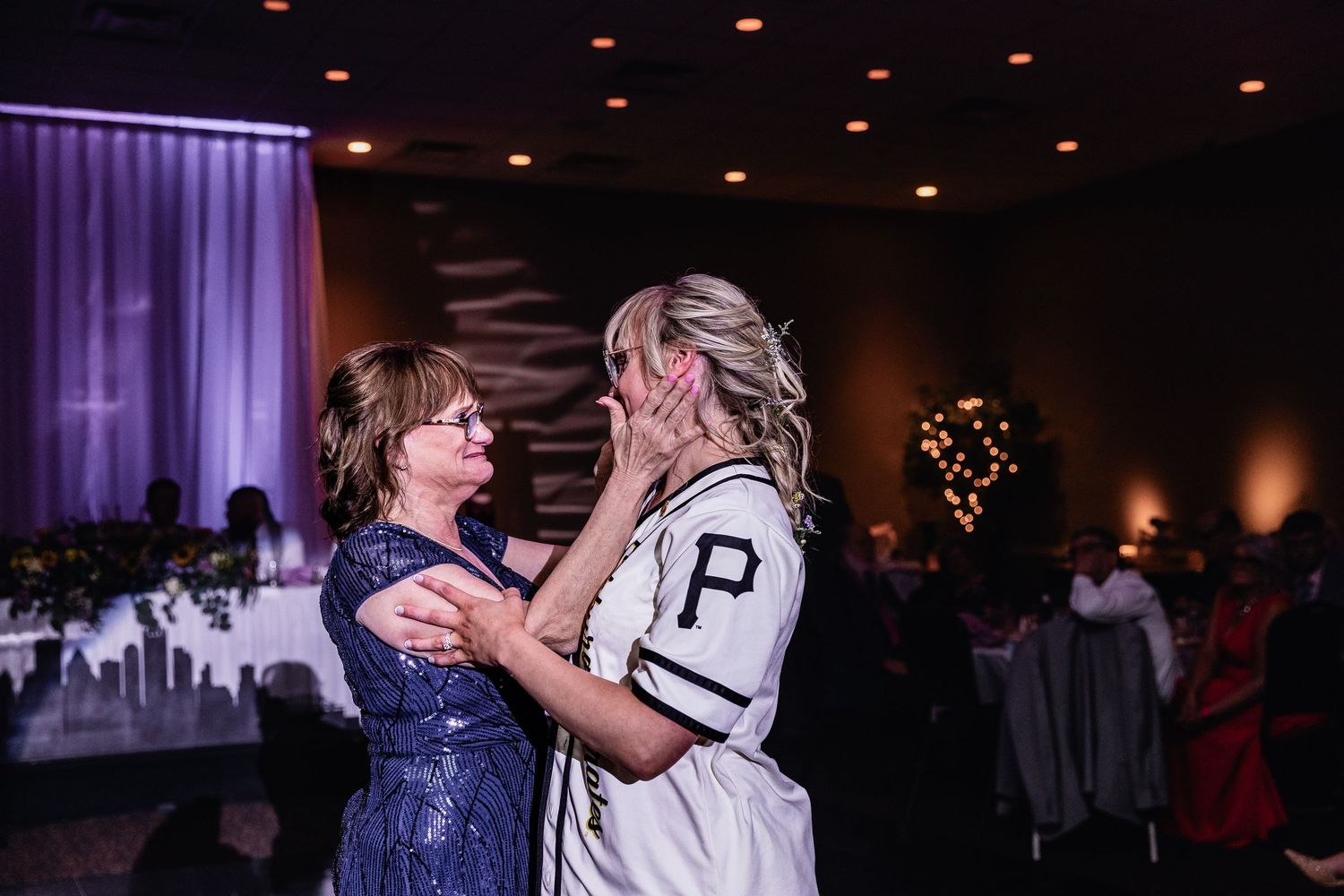 An emotional moment shared between two people embracing at an elegant indoor wedding reception with purple lighting.