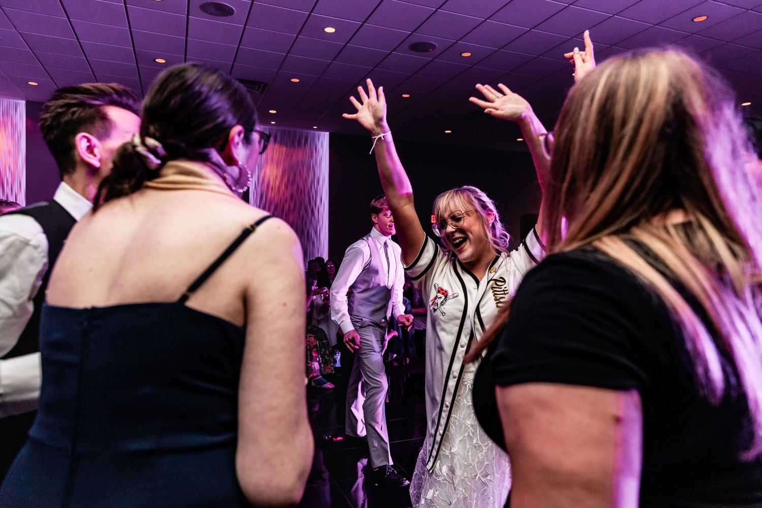 People dancing and having fun at a party with purple lighting in a dark venue interior.