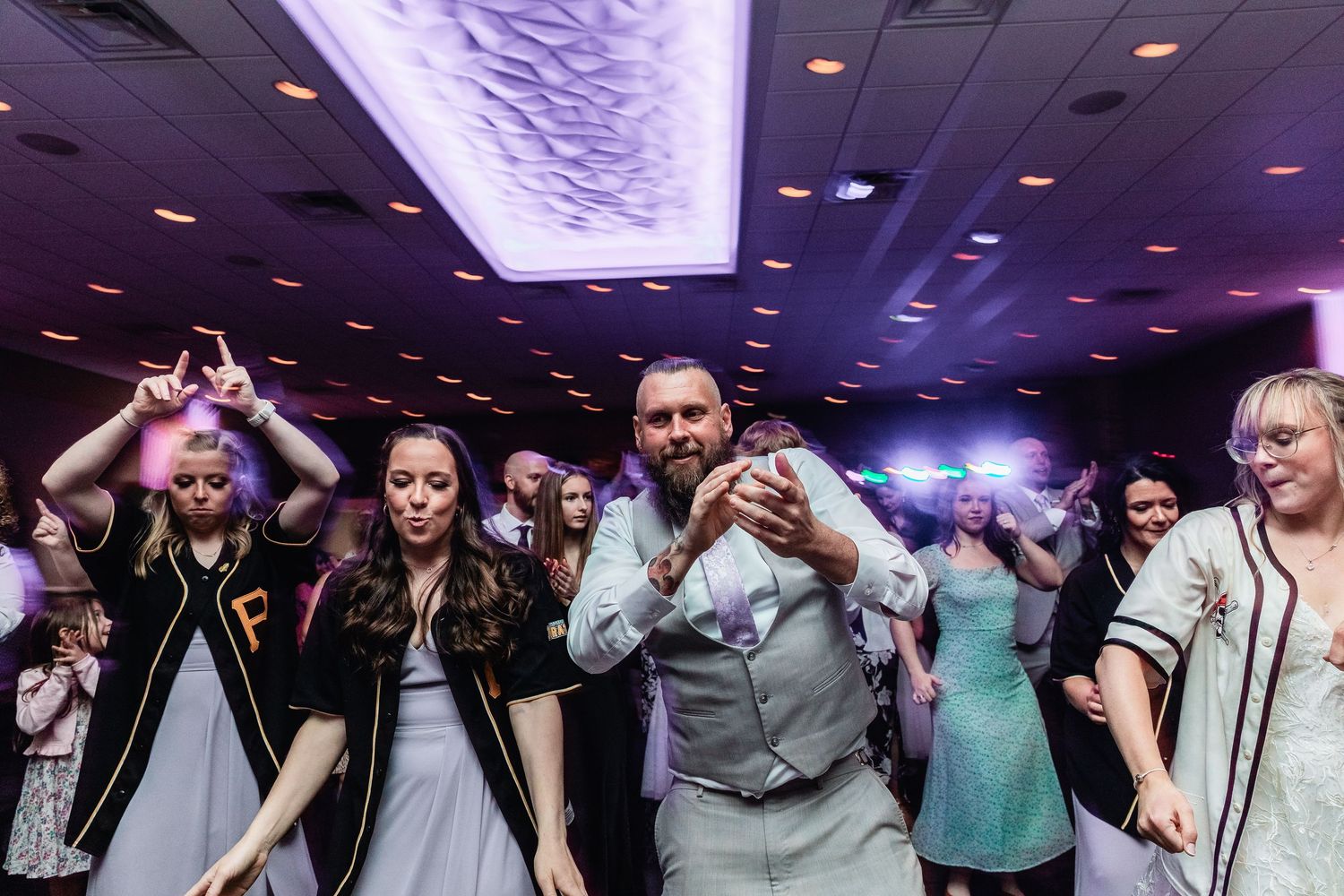 Wedding party guests dancing and having fun on a dance floor illuminated by purple lighting at a reception.