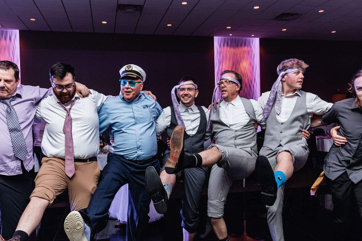 Group of wedding party guests line up in a fun dance pose showing their socks and legwear against a purple backdrop.