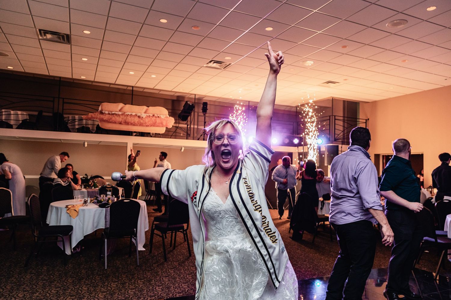 Guest dances with arms raised in celebration at an indoor wedding reception with round tables and guests in the background.