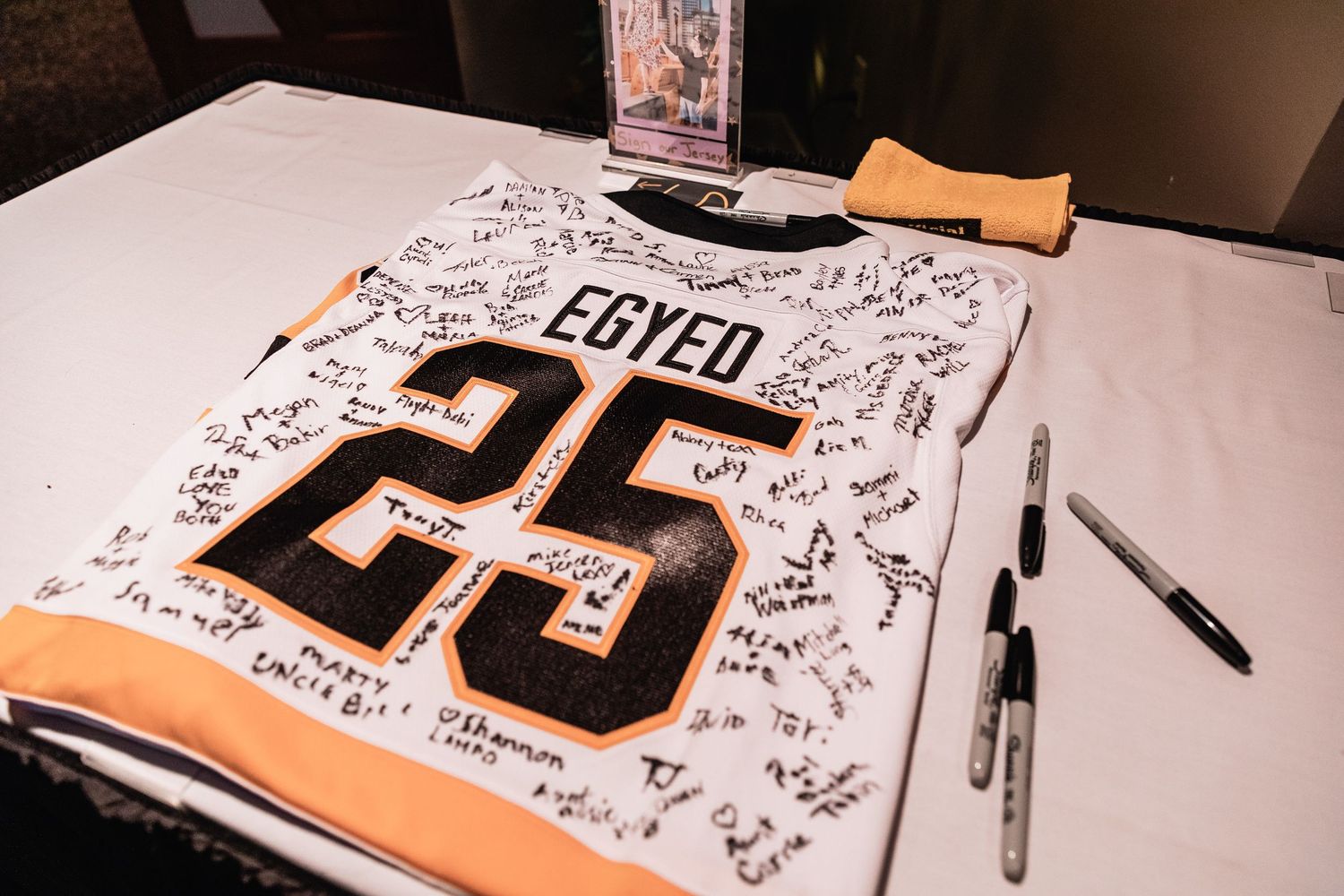 A white sports jersey with number 25 covered in signatures and black markers laying on a dark surface.