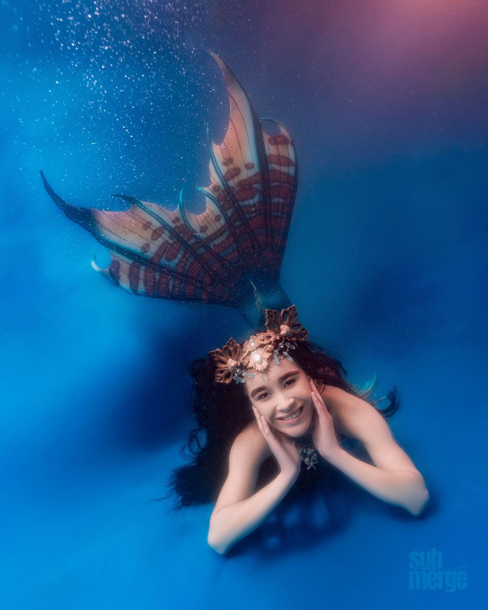A fantasy-themed underwater scene with flowing hair and glitter against a deep blue backdrop, creating a dreamy atmosphere.