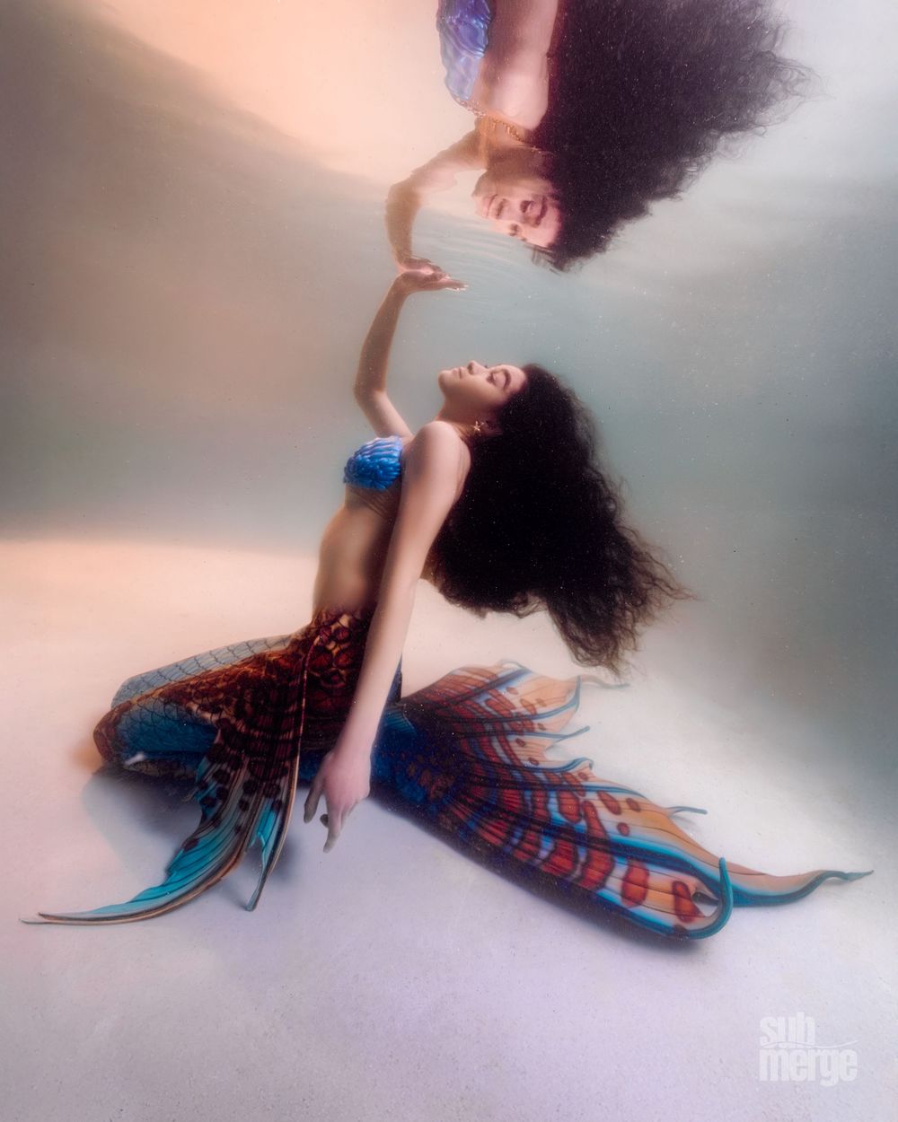 Two underwater figures with flowing dark hair dance gracefully in a dreamy artistic portrait composition.