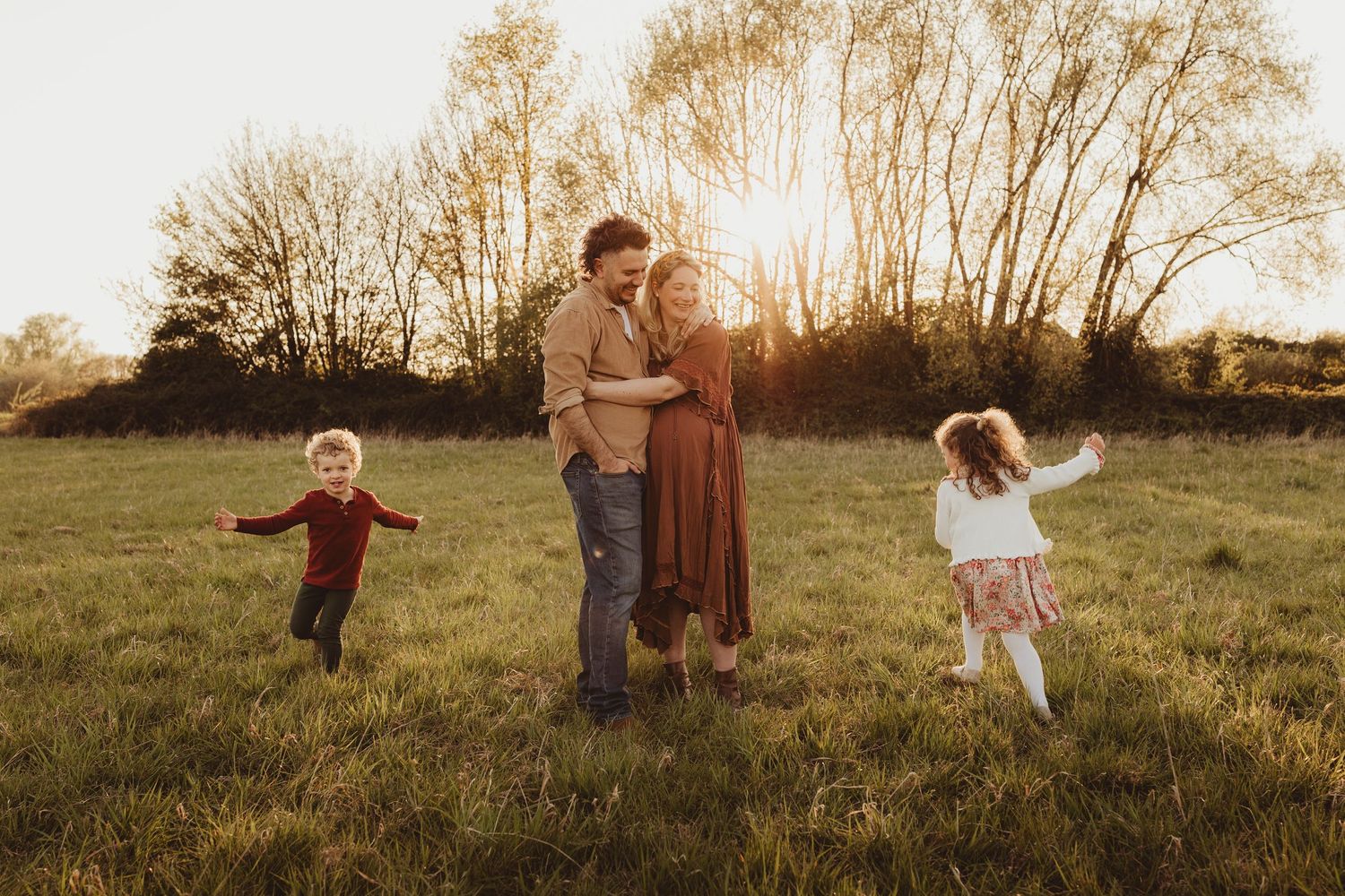 A loving family plays together in a golden autumn field at sunset as two children run playfully nearby.