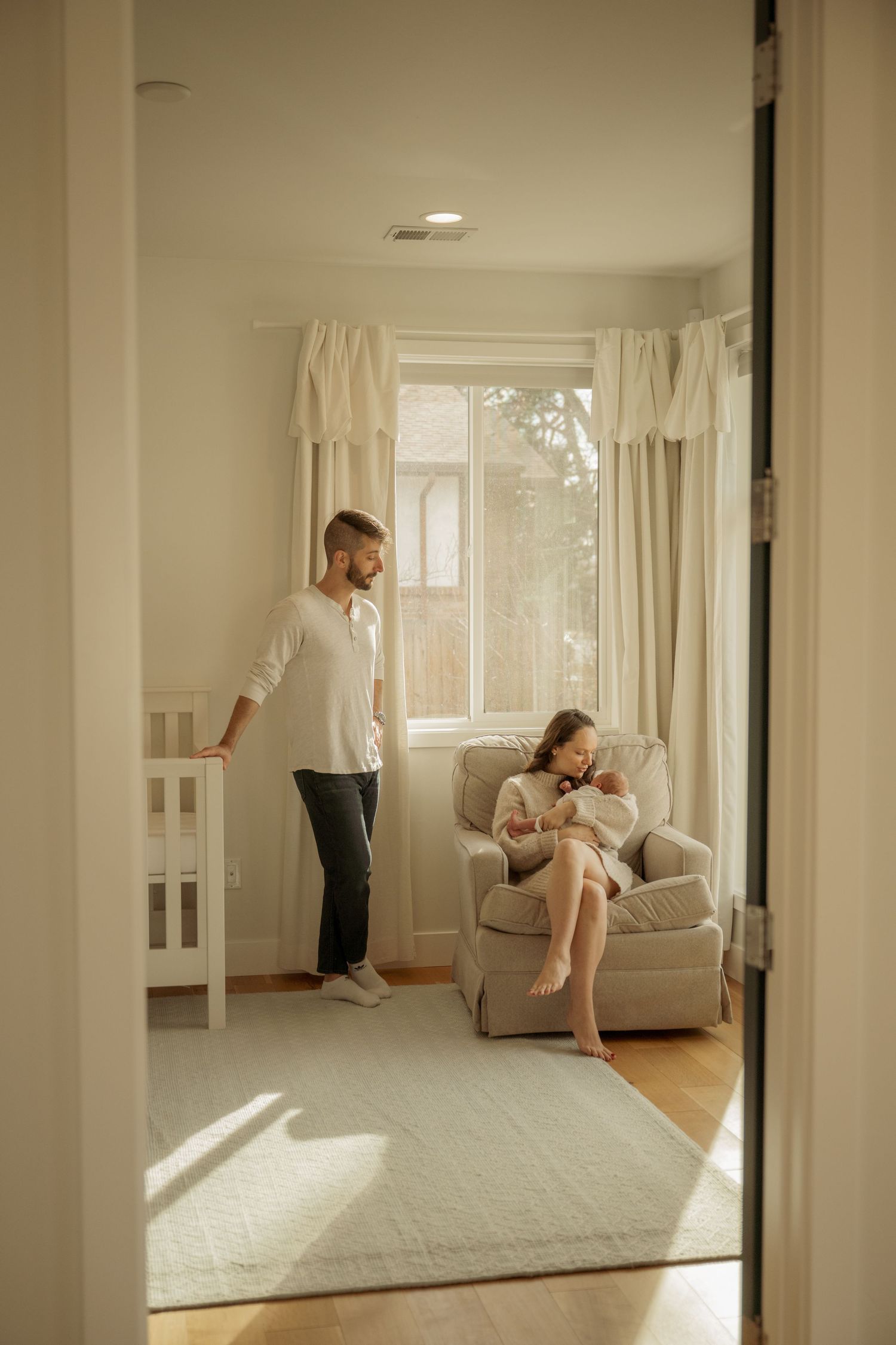 A couple shares an intimate moment by a window with soft natural light creating a warm romantic atmosphere.