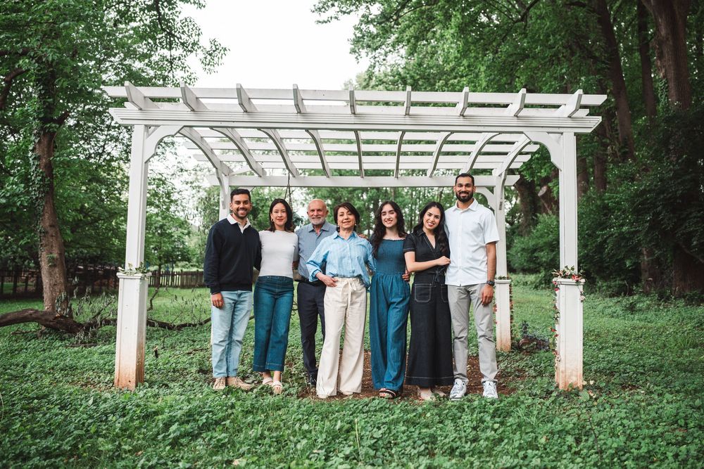 A group of people standing together under a white garden pergola in a lush green outdoor setting.