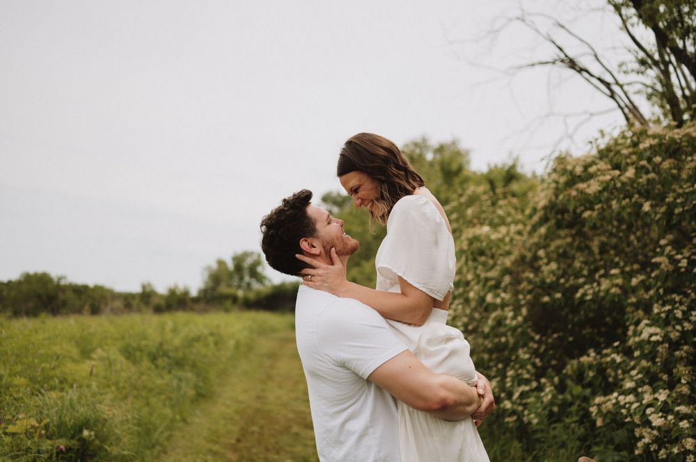 A joyful couple shares an intimate moment on a countryside path with blooming flowers.