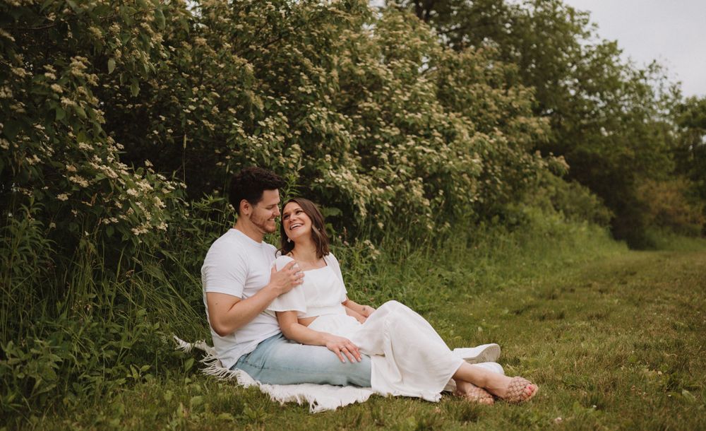 A tender moment between a couple sitting on a blanket against a backdrop of green foliage.