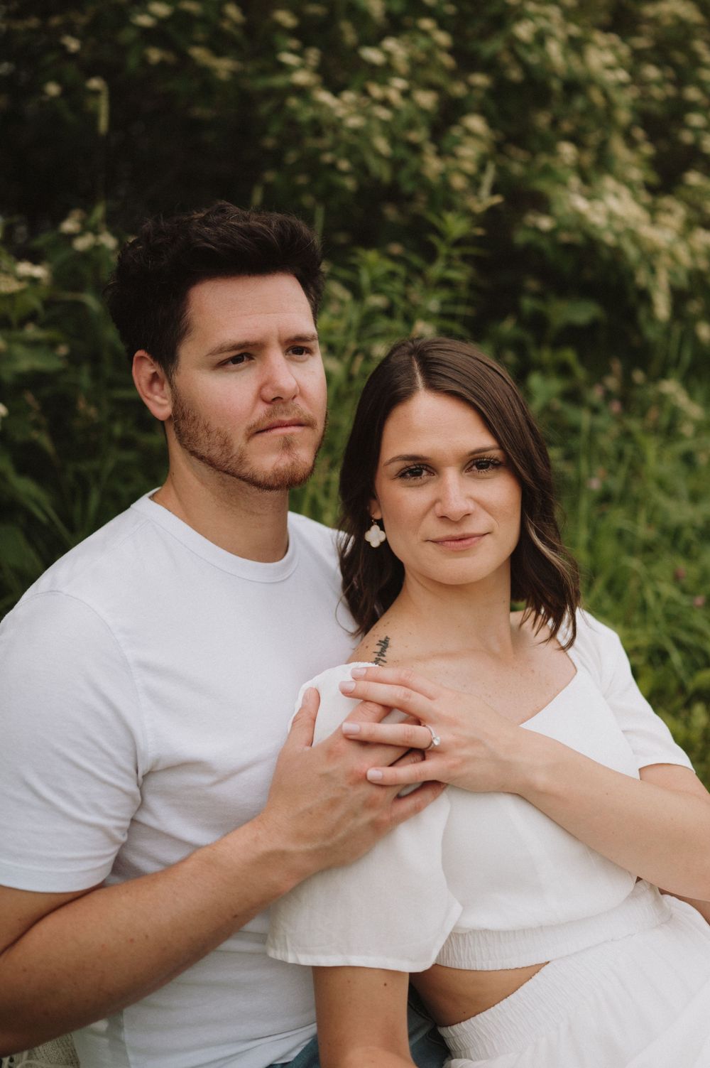 A close-up portrait of a couple in white attire against a natural green background.