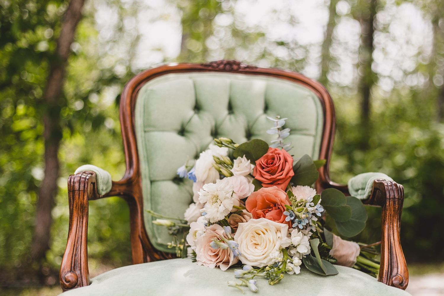 Elegant vintage tufted mint green armchair with coral and blush pink rose bouquet in outdoor garden setting.