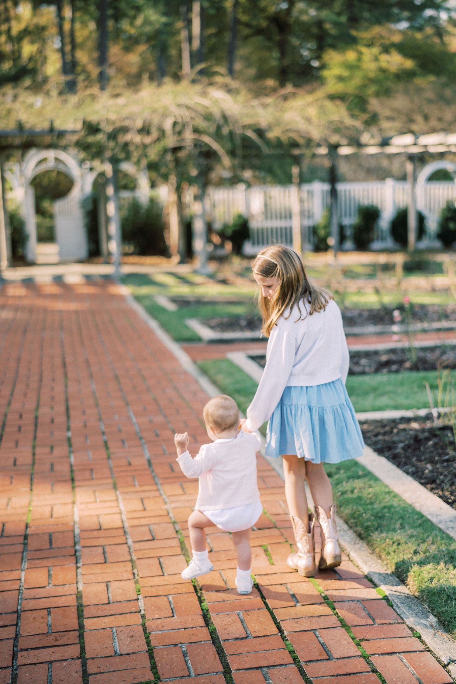 Parent and child walking hand-in-hand along brick path near garden arches.