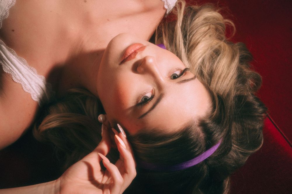 Dreamy vintage portrait with soft lighting and blonde wavy hair against red backdrop.