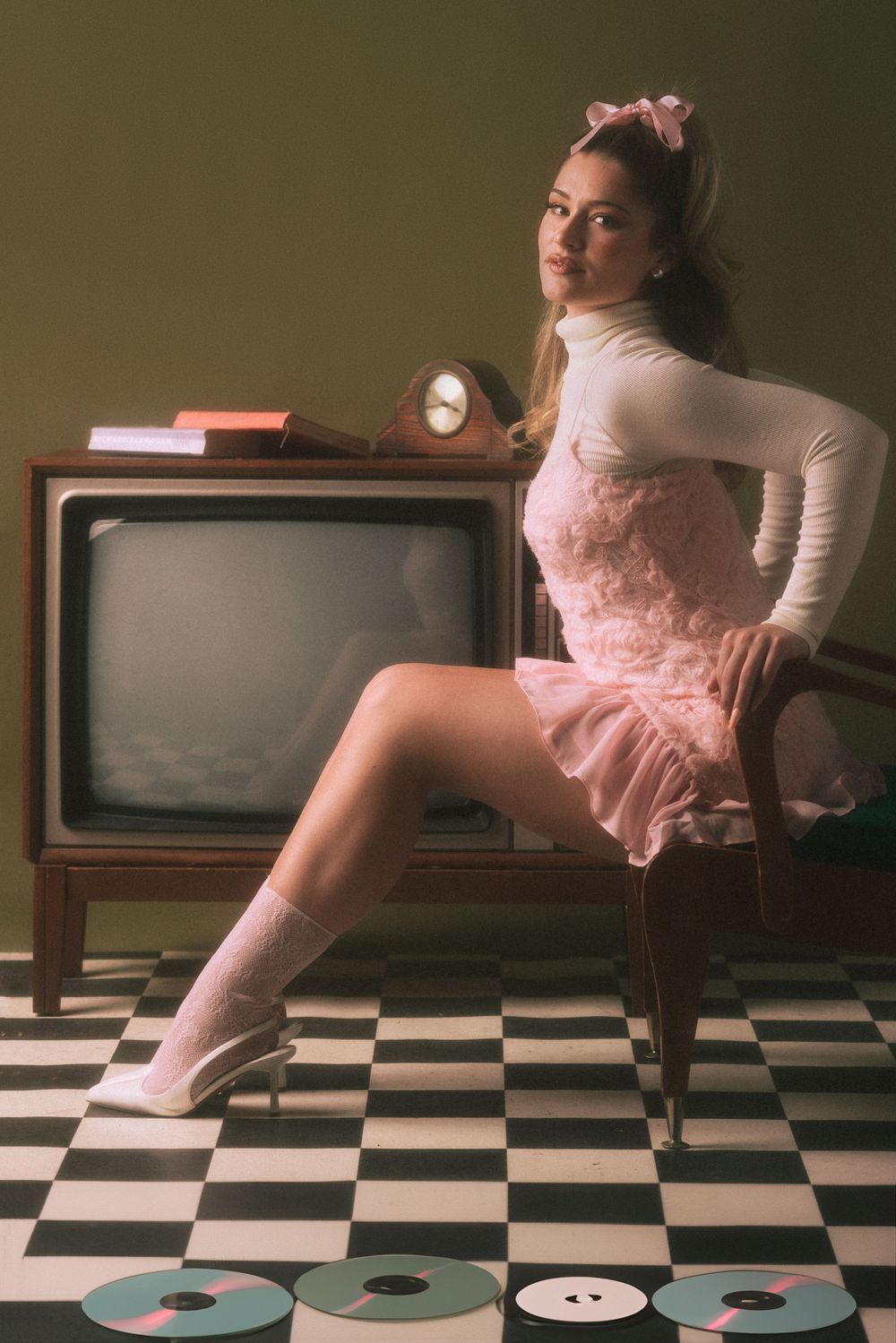 Vintage-inspired photo with pink dress and bow sitting on retro TV set with vinyl records.