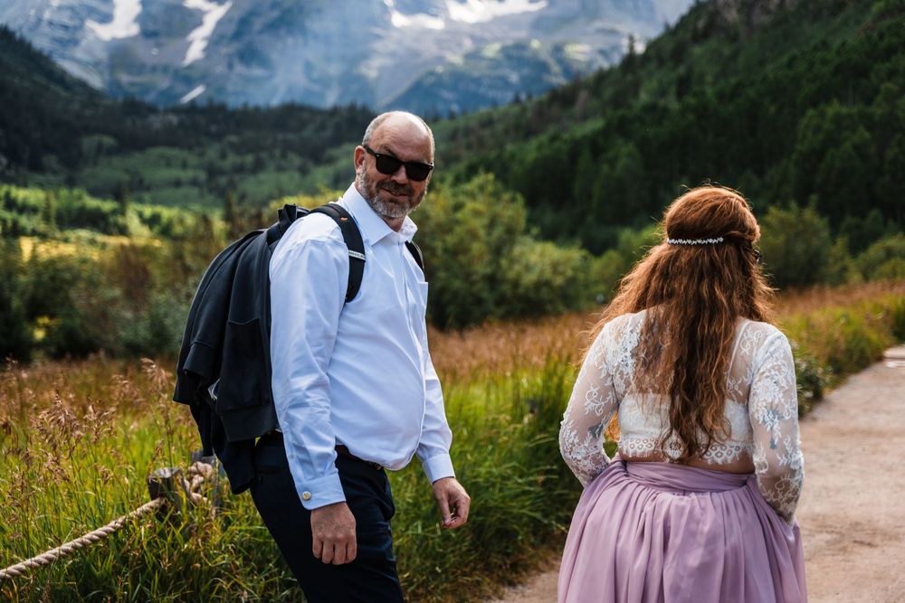 Two people hiking on a mountain trail with stunning peaks and valley views in the background.