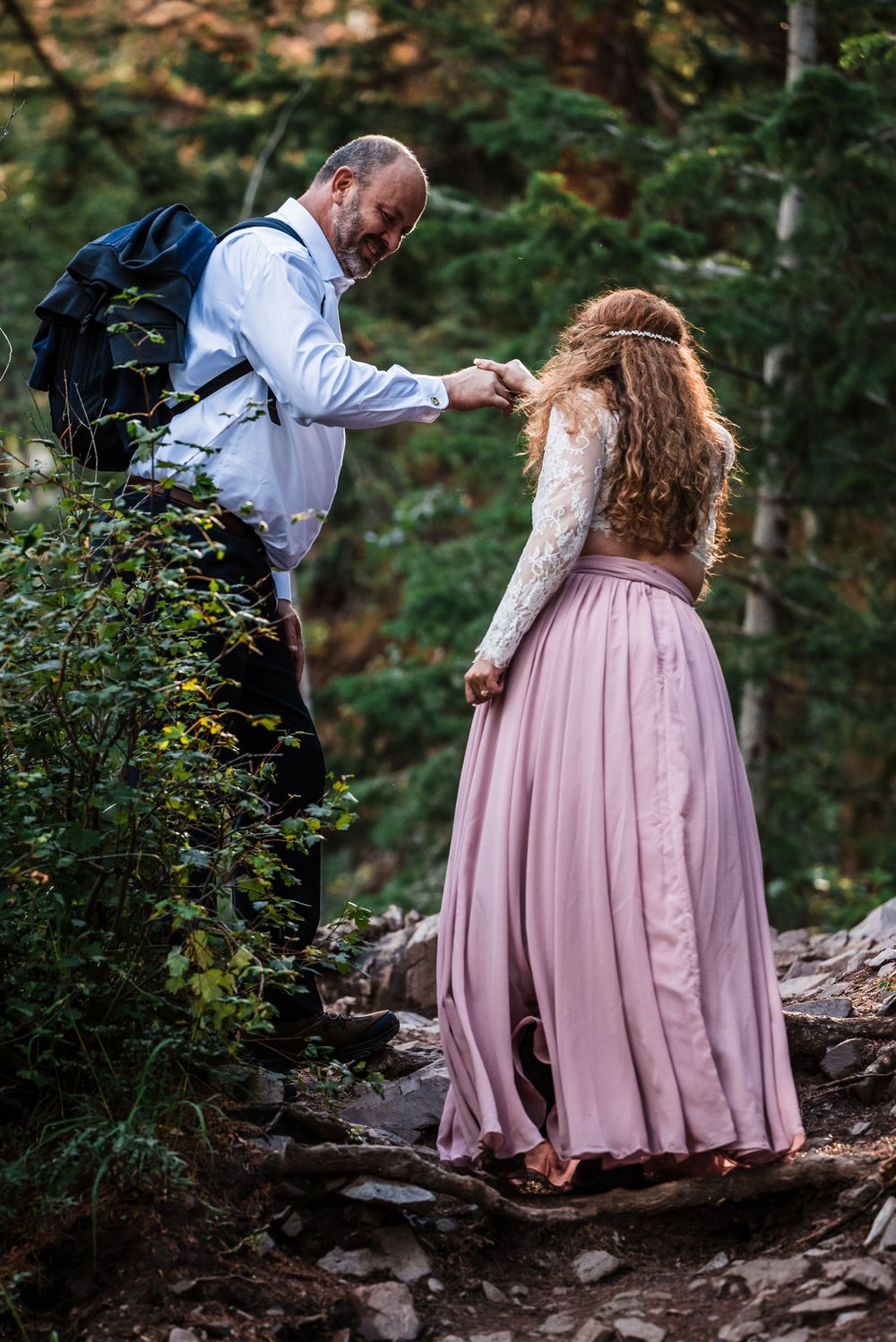 A couple navigating rocky mountain terrain together on a hiking trail through wilderness.