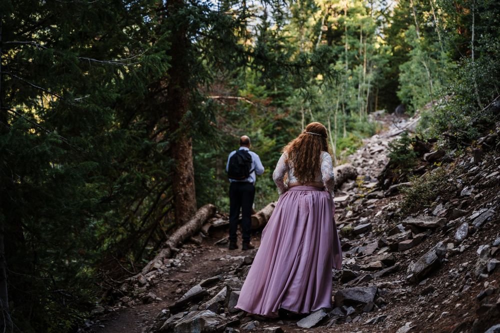 Hiking couple traverse rocky mountain path wearing formal attire.