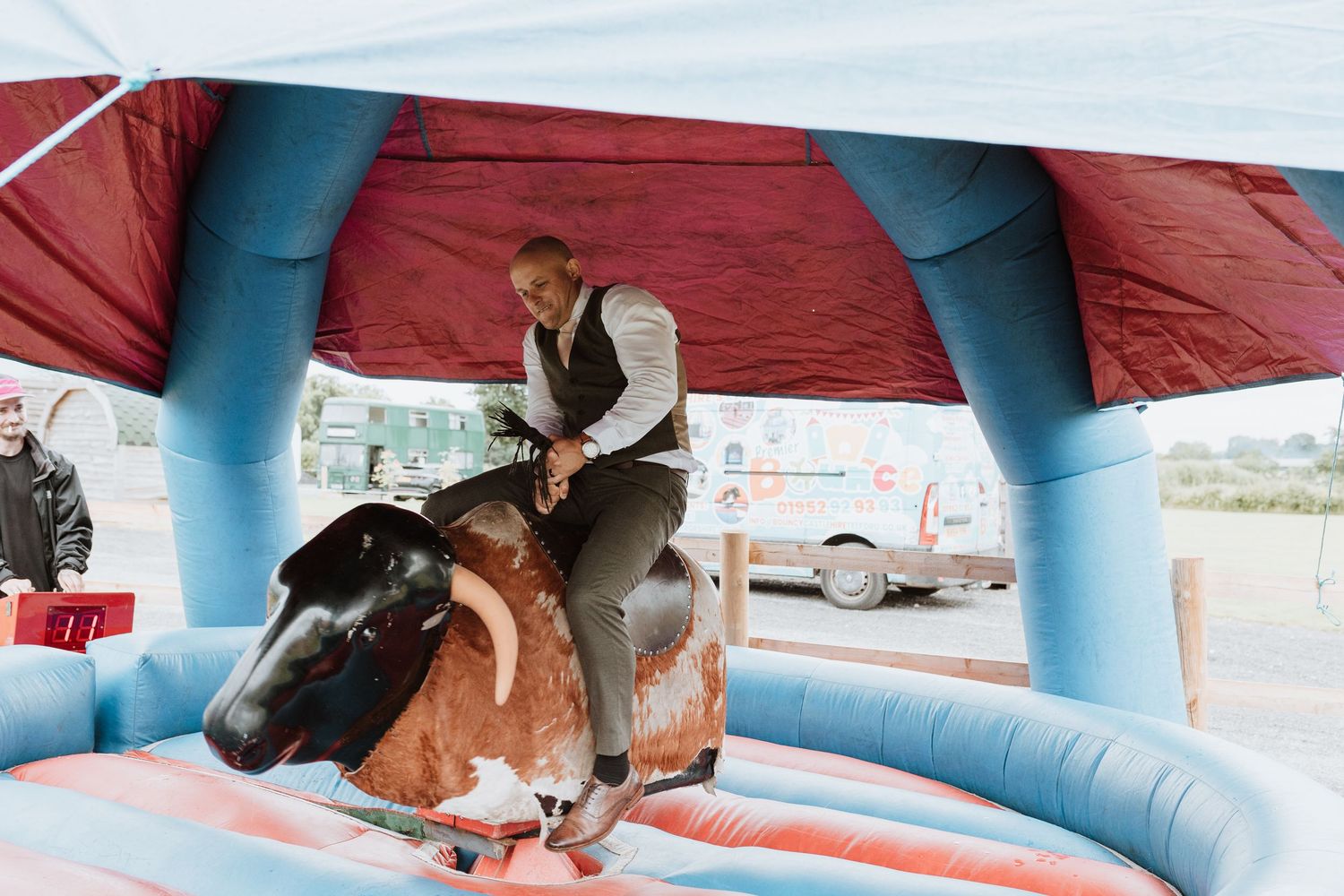 A determined groom rides a mechanical bull on an inflatable blue and red bouncy platform at Wedding Reception