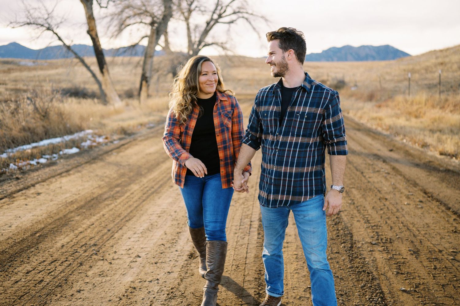 Couple walking and laughing together on dirt road through winter grassland.