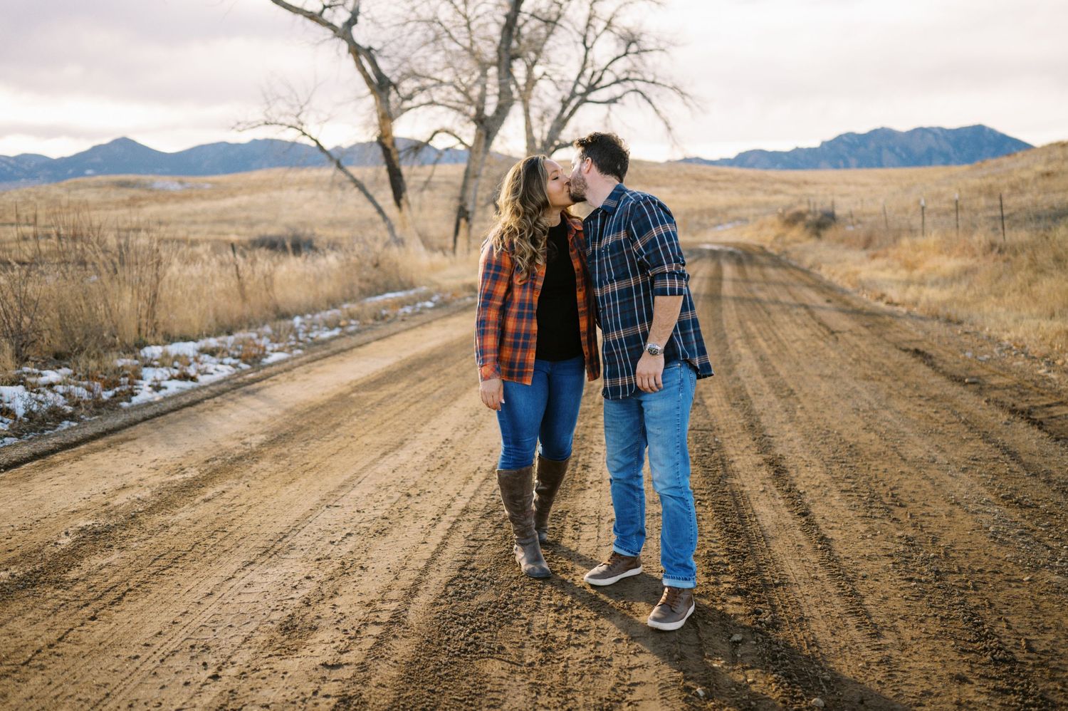 Couple strolling down rural dirt road with bare trees and mountains in distance.