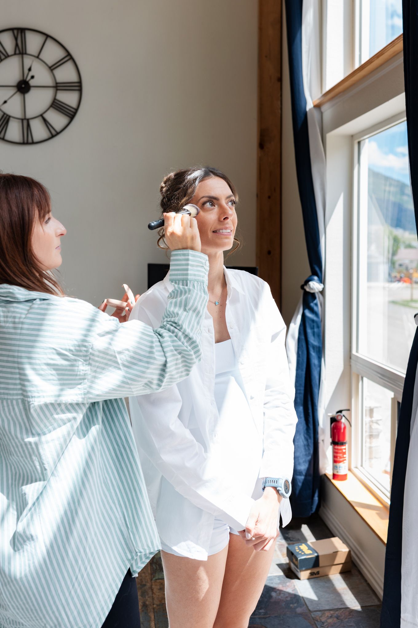 Getting ready scene with hair and makeup preparations near a large window with natural light.