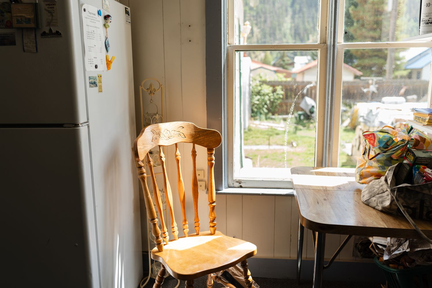 Empty wooden chair near window and refrigerator in a sunlit kitchen space, turned getting ready room.