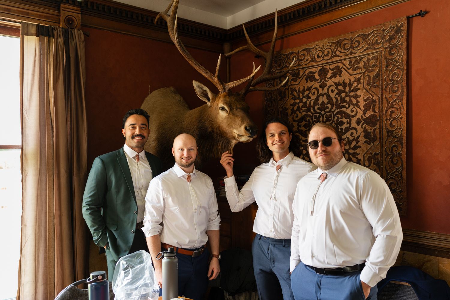 Group photo in formal attire with mounted deer head in elegant wood-paneled room.