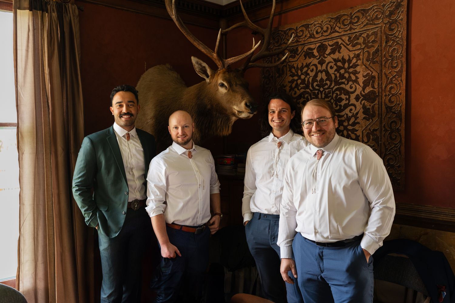 Formal gathering in front of mounted deer head in rustic room with red walls.