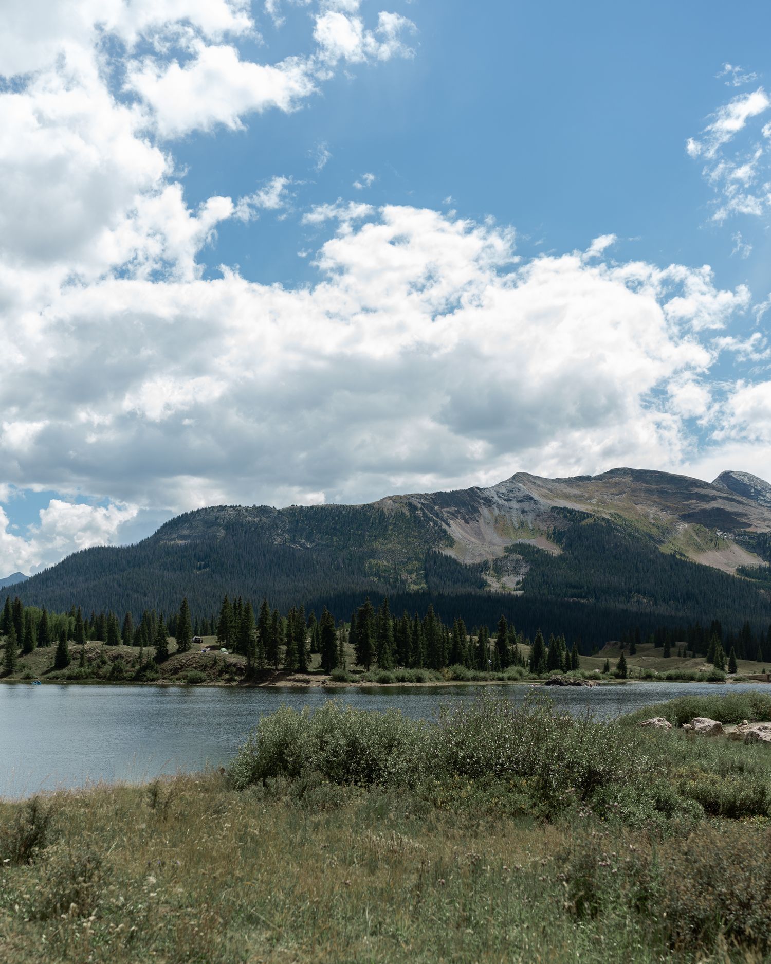 Scenic mountain landscape with lake and evergreen forest under bright blue sky.