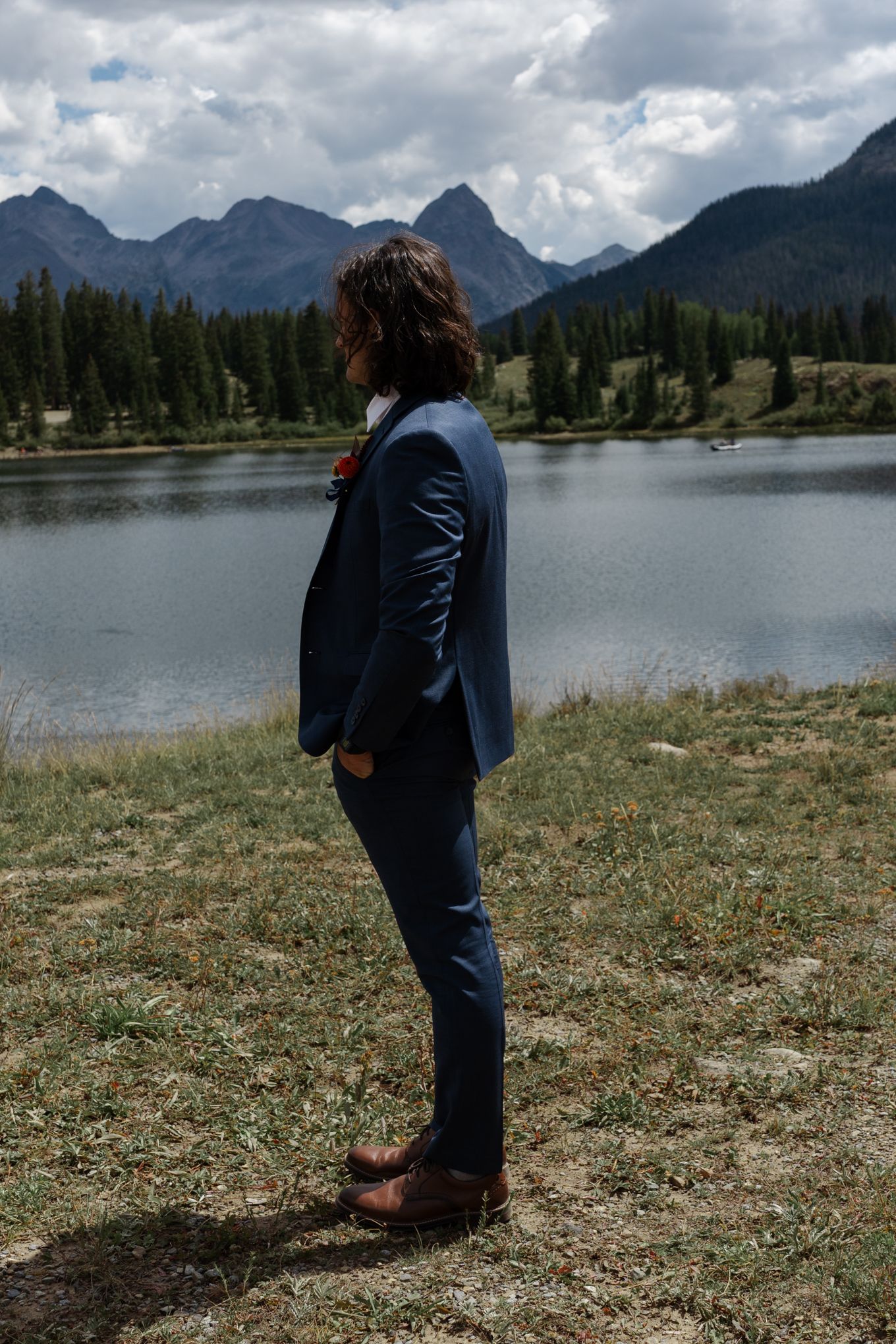 Mountain vista with lake view and figure in blue suit standing on shoreline.
